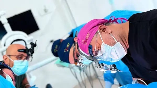 Dentist placing a dental implant under direct mentor supervision during live-patient surgical training